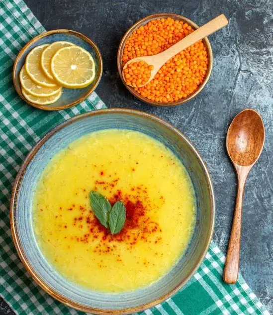 Shorbat Adas, une soupe de lentilles corail épicée servie dans un bol avec un filet de citron et de la coriandre fraîche.